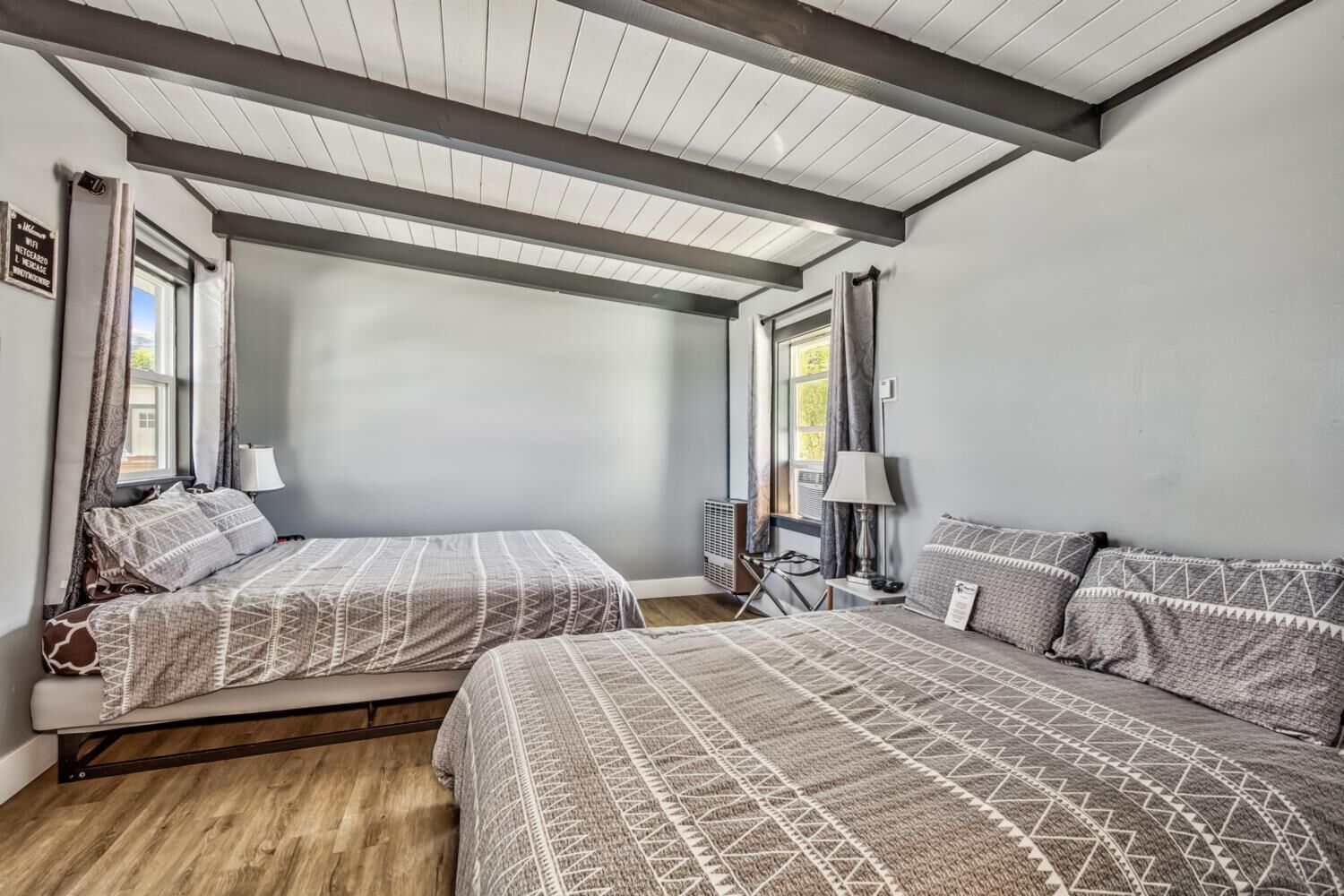 A room with two beds, a wooden floor, and a sloped ceiling with exposed beams.