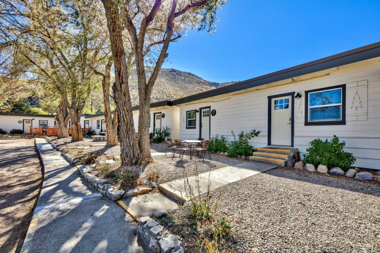 A single-story building with a front porch, a small outdoor seating area, and a gravel driveway.