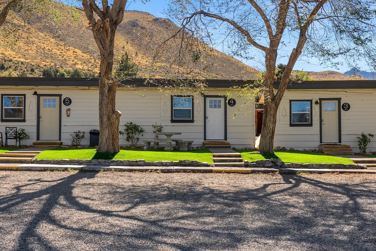 A row of white mobile homes with numbered doors, set against a backdrop of hills.