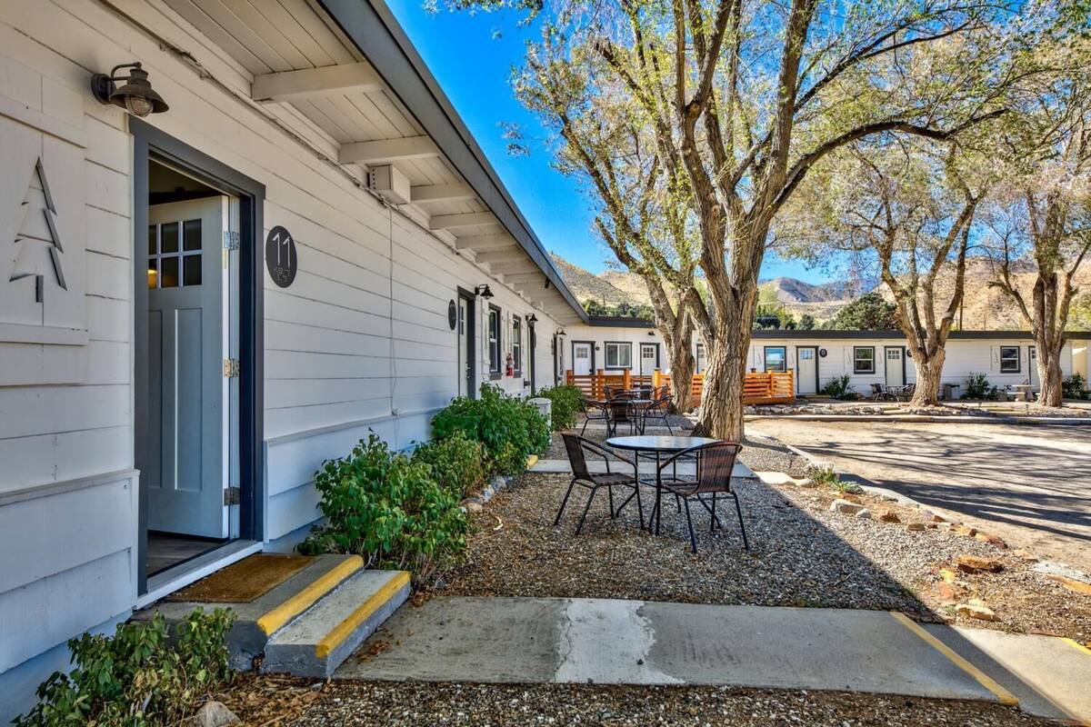 A white building with a door, steps, and a patio with tables and chairs.