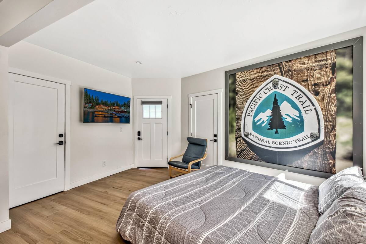 A bedroom with a bed, a chair, a door, and a wall with a scenic poster.