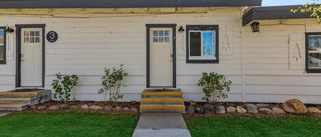 A single-story house with a front porch, numbered doors, and a small garden area.