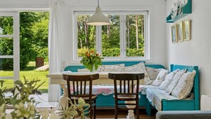 Een gezellige kamer met een houten tafel, twee stoelen, een blauwgroene bank en een raam met uitzicht op groen.