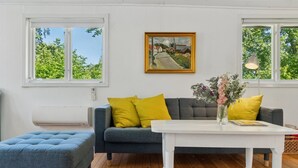 Een moderne woonkamer met een grijze bank, gele kussens, een witte salontafel en een kleurrijk gestreept vloerkleed.