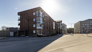 A modern multi-story building with a mix of brick and glass facades, a clear sky, and a wide road in the foreground. - Metsämansikan helmi I Free parking, WiFi and Netflix (Espoo)