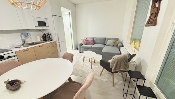 A modern kitchen with white cabinets, a dining table with pink chairs, a grey sofa, and a small black table. - Metsämansikan helmi I Free parking, WiFi and Netflix (Espoo)