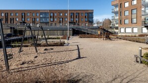A playground with swings and a climbing structure, surrounded by a gravel area and buildings in the background. - Metsämansikan helmi I Free parking, WiFi and Netflix (Espoo)