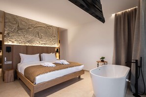 A modern hotel room with a large bed, a wall-mounted artwork, a small table with a plant, and a large bathtub.