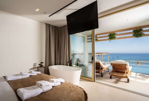 A modern bedroom with a large bed, a bathtub, and a balcony with lounge chairs.