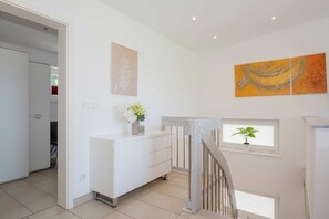 A modern interior with a white staircase, a small window with a plant, and a white cabinet with a vase of flowers.