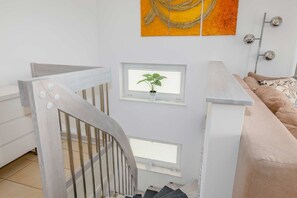 A staircase with a railing, a window with a plant, a sofa, and a wall with a decorative piece.