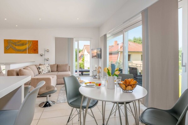 A modern living room with a sofa, dining table, chairs, and a balcony with a view.