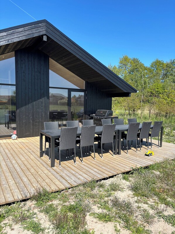 Un espace de restauration extérieur moderne, doté d’une terrasse en bois, d’une véranda en verre et d’un barbecue.