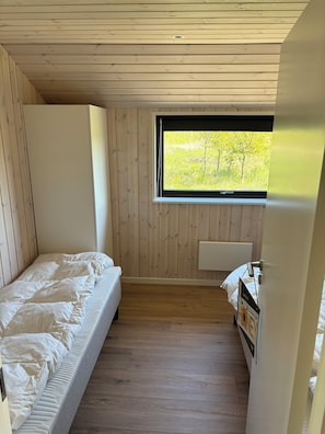Een houten kamer met een bed, een raam en een radiator.