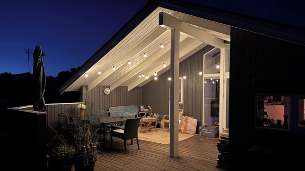 A covered outdoor patio with a dining area, seating, and a view into the house. - Cosy summer house at Kobæk Strand (Skælskør)