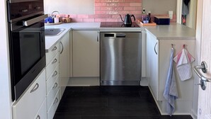 A compact kitchen with white cabinets, a stainless steel dishwasher, and a black oven. - Cosy summer house at Kobæk Strand (Skælskør)