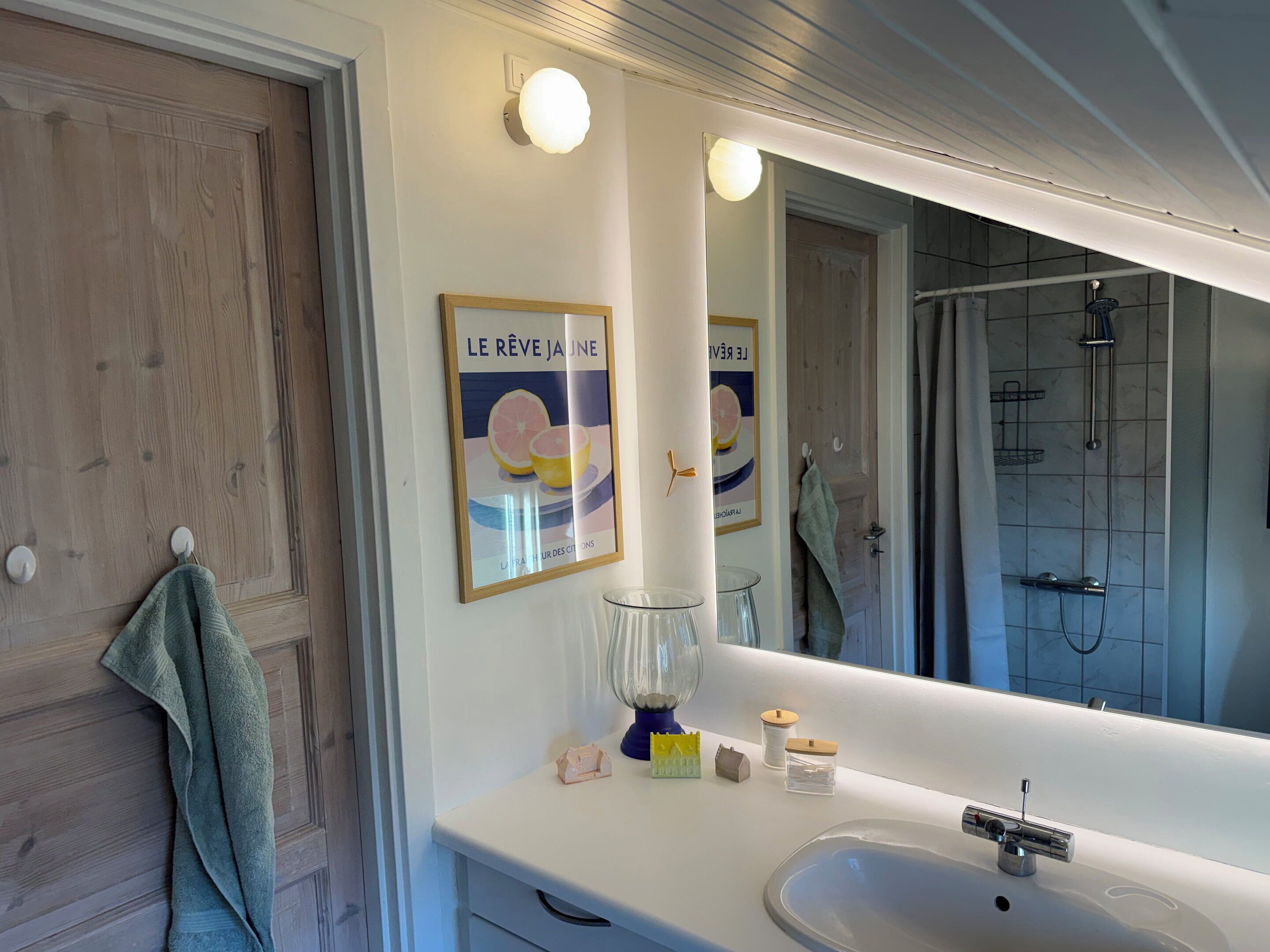 Une salle de bain avec un grand miroir, un lavabo, une douche et une serviette accrochée au mur.