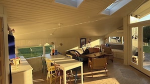 A spacious living area with a high ceiling, skylights, a dining table, and a sofa.
