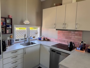 Cozinha com armários brancos, lava-louças de aço inoxidável, máquina de café e janela com vista para um estacionamento.