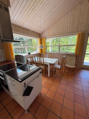 A kitchen with a stove, dining table, chairs, and large windows with curtains.