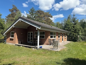 A single-story brick house with a covered porch, a small outdoor seating area, and a grassy yard.