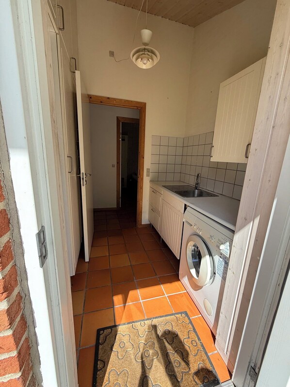 A kitchen with a washing machine, a sink, and a door leading to another room.