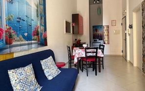 Una habitación con sofá, mesa de comedor, sillas y un cuadro de un paisaje marino.