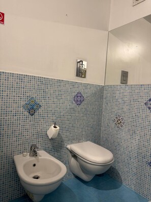 A bathroom with a bidet, toilet, and a wall-mounted light fixture.
