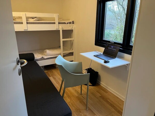 A room with a bunk bed, a desk with a laptop, and a window.
