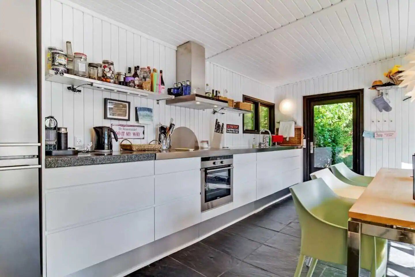 Ett modernt kök med vita köksskåp, en inbyggd ugn och en matplats med bord och stolar.