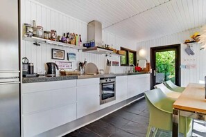 Una cocina moderna con armarios blancos, horno empotrado y comedor con mesa y sillas.