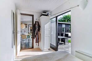 A narrow hallway leading to a dining area with a table and chairs, a coat rack, and a sliding glass door to an outdoor patio.