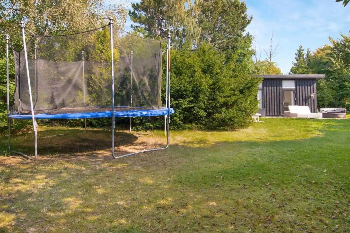 A trampoline with a safety net in a grassy yard with a shed in the background.