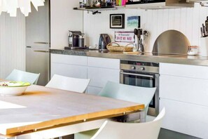Eine moderne Küche mit weißen Schränken, einem Edelstahlbackofen und einem Essbereich mit einem Holztisch und weißen Stühlen.