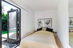 Ein Schlafzimmer mit einem Bett, einer Tür, die auf einen Balkon führt, und einer Wand mit einem gerahmten Bild.