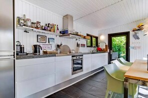 Et moderne køkken med hvide skabe, indbygget ovn og spiseområde med bord og stole.