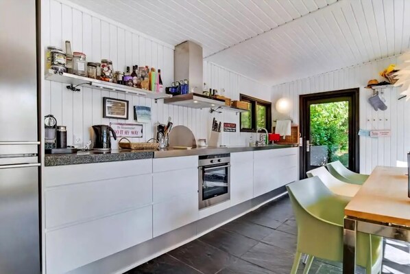 A modern kitchen with white cabinetry, a built-in oven, and a dining area with a table and chairs.