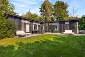 Et moderne hus med en terrasse, der har et bord, stole og en sofa.