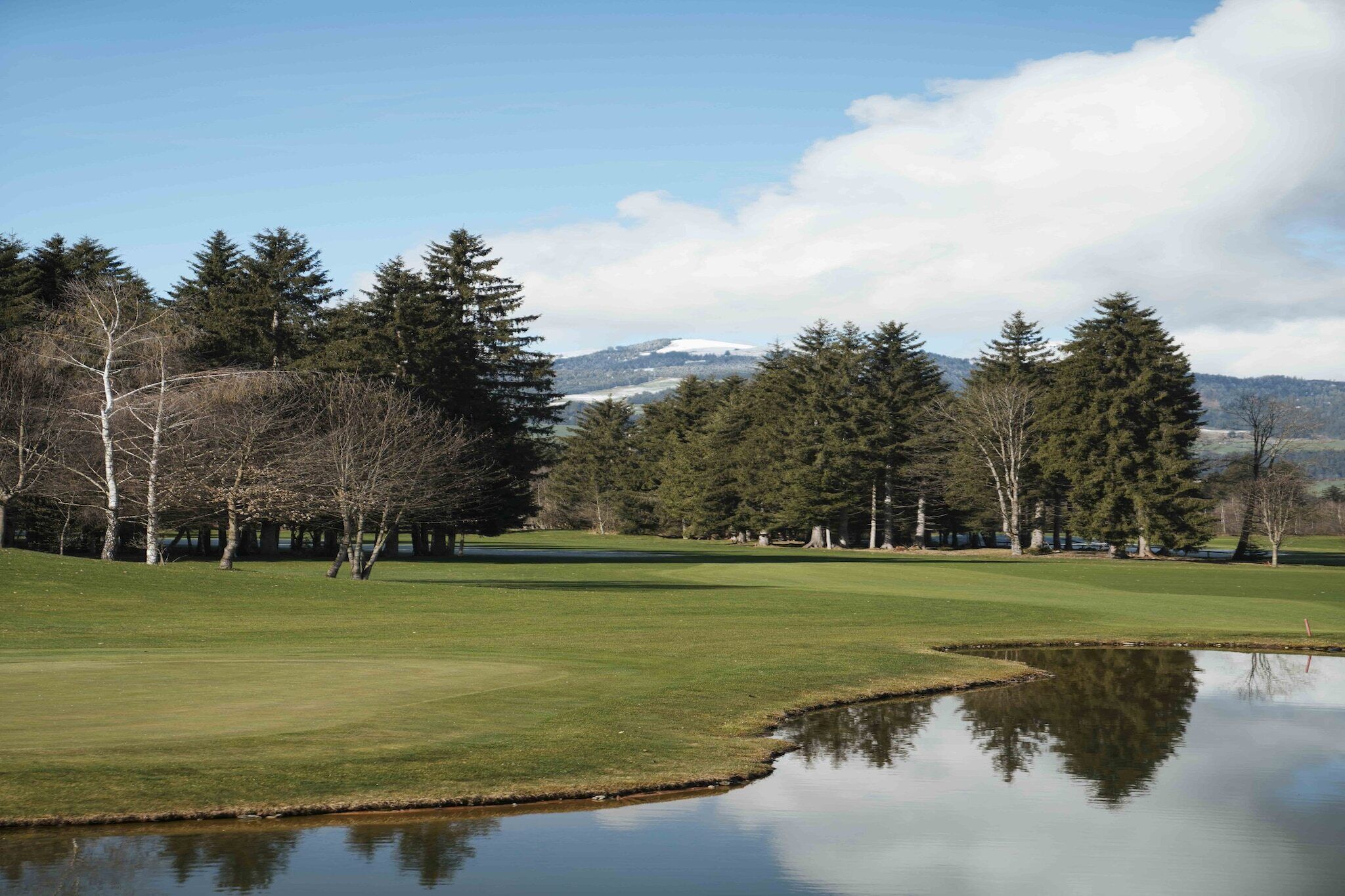A golf course with a pond, trees, and a mountain in the background.