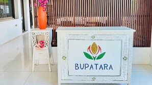 Un mostrador de recepción con un logo que dice "BUPATARA" y un jarrón decorativo con flores rosas.