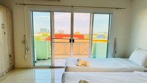 Una habitación de hotel con un gran ventanal corredero que da a un balcón, una cama con ropa blanca y un armario.