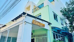 Un edificio de dos pisos con fachada verde y blanca, una entrada visible con reja metálica y un letrero con texto.