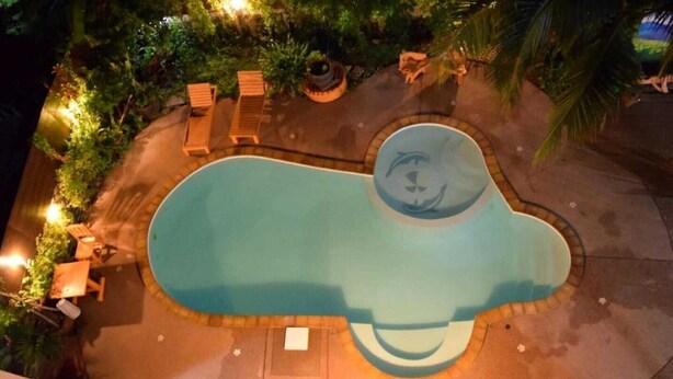 Vista aérea de una piscina de forma singular, rodeada de sillas de descanso y plantas en macetas.