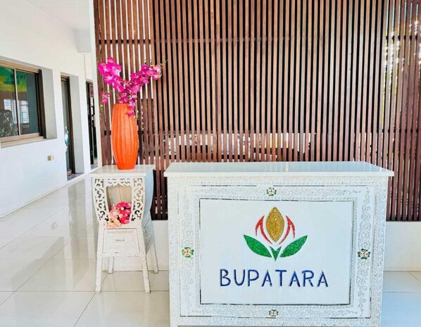 Un comptoir d’accueil orné du logo « BUPATARA » et un vase décoratif contenant des fleurs roses.