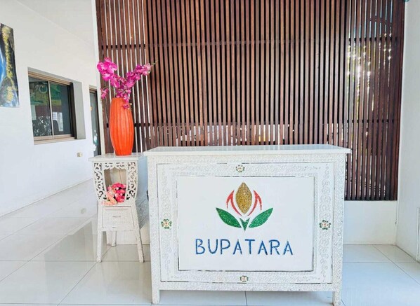 A reception desk with the name 'BUPATARA' and a logo, a small white chair, a vase with pink flowers, and a wooden slatted background. - Double Room | Great for Couples on a Budget (Unknown)