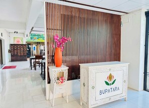 Zona de recepción con un separador de madera, una consola blanca con el logo 'BUPATARA' y un florero con flores rosas.