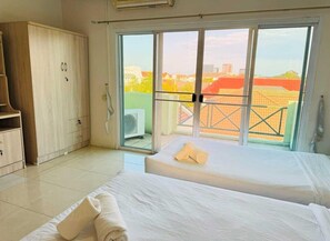 A hotel room with two beds, a wardrobe, and a balcony with a city view.