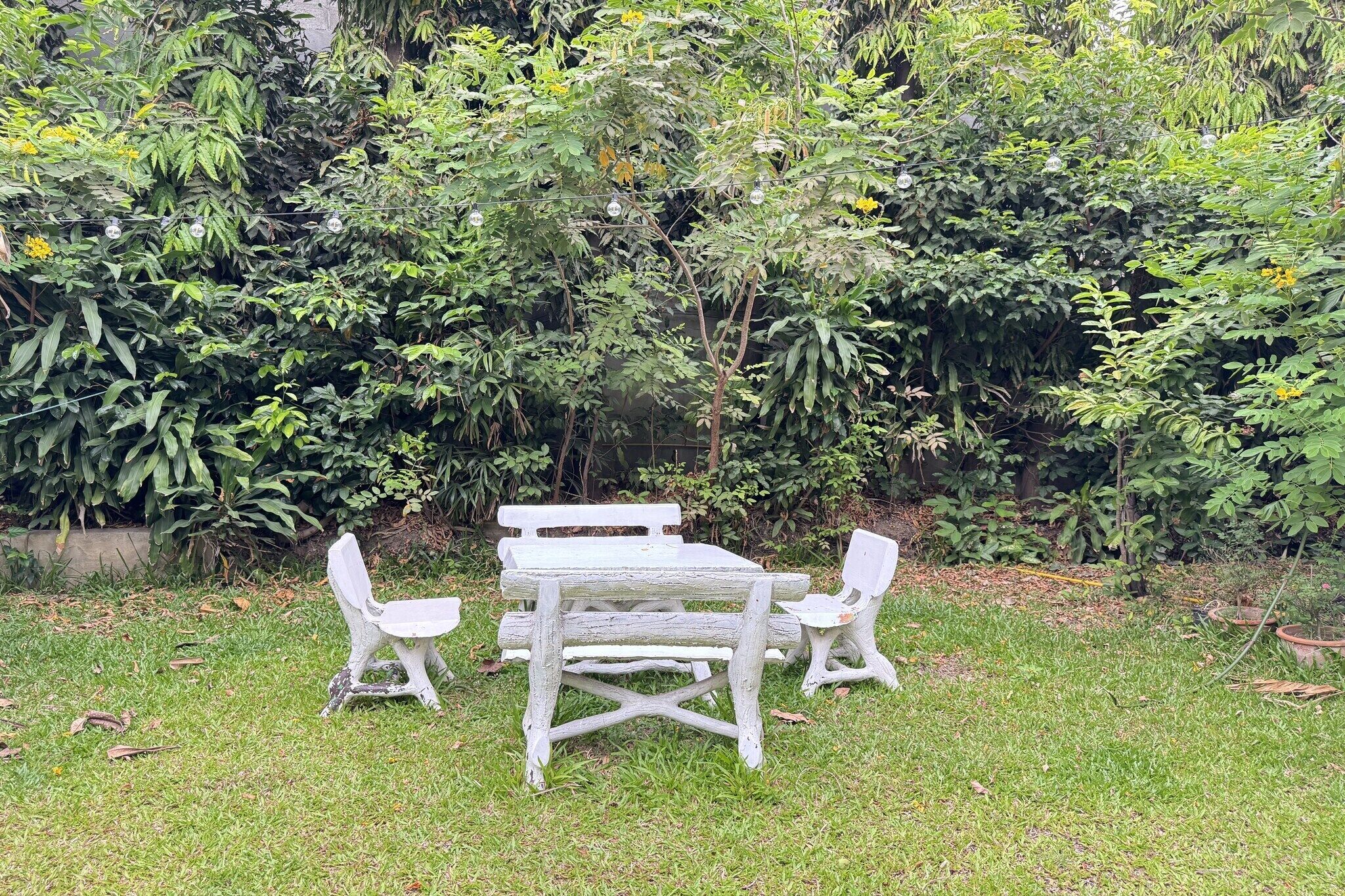 A rustic outdoor seating area with a wooden table and chairs surrounded by lush greenery.