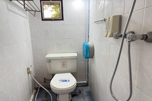A small, tiled bathroom with a toilet, a hand dryer, and a shower hose.