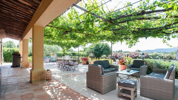 Une terrasse extérieure aménagée avec des meubles en osier, un barbecue et une vue sur un vignoble.
